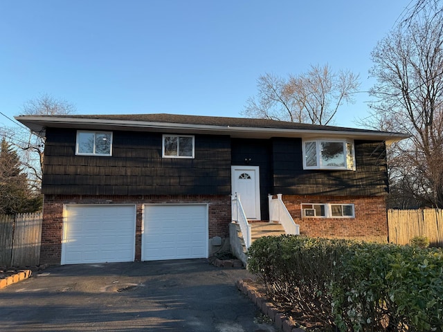 raised ranch featuring brick siding, driveway, and fence