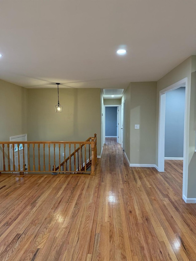 hallway with an upstairs landing, attic access, baseboards, and wood finished floors