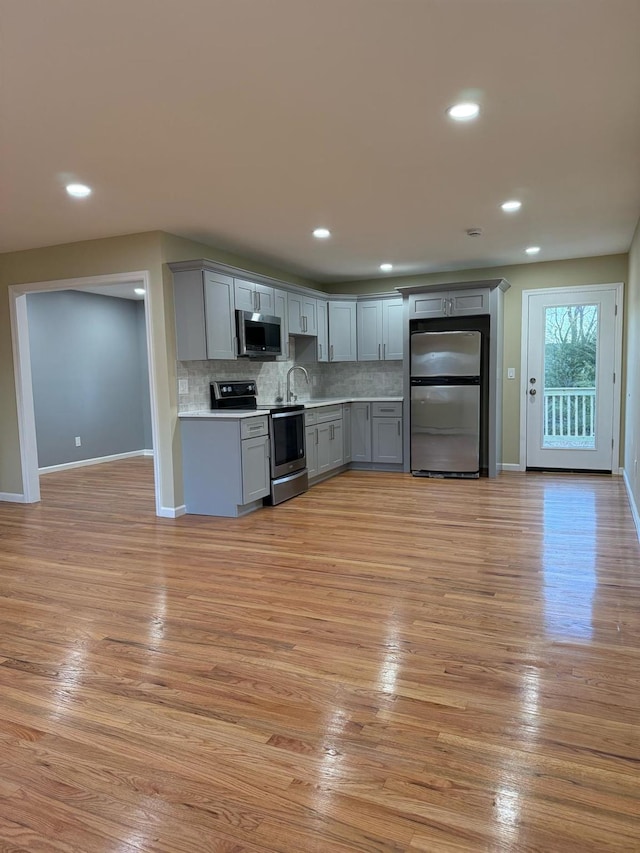 kitchen with tasteful backsplash, light wood finished floors, gray cabinetry, and stainless steel appliances