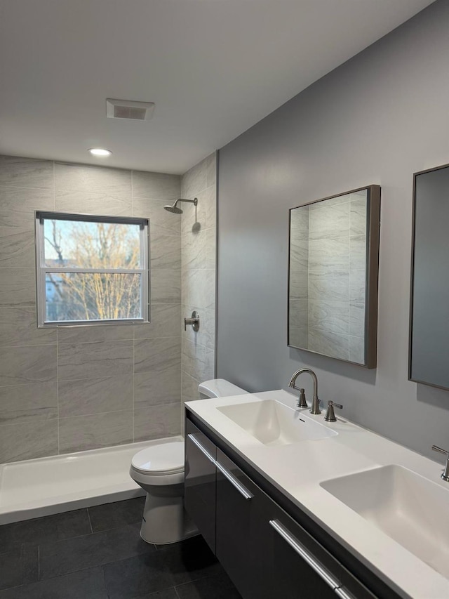 full bath featuring double vanity, tiled shower, toilet, and a sink