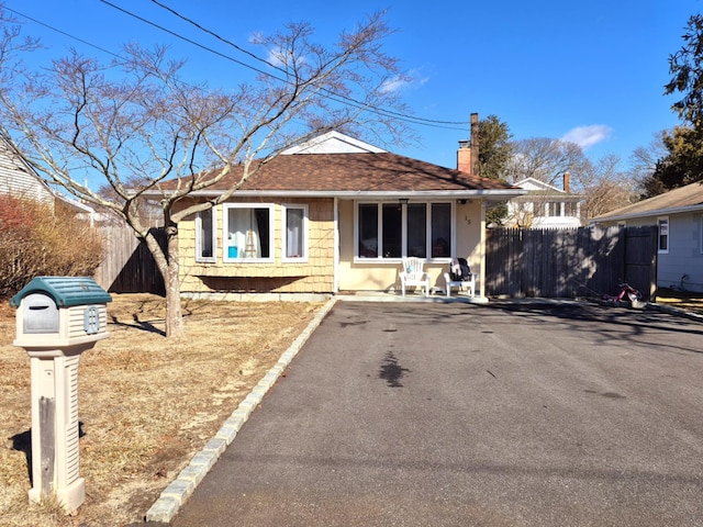 view of front facade with driveway, a chimney, fence, and roof with shingles