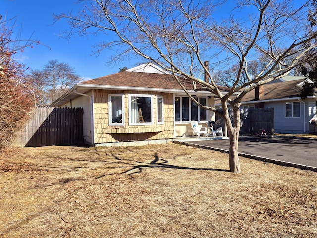 view of front of house featuring driveway, a patio area, fence, and roof with shingles