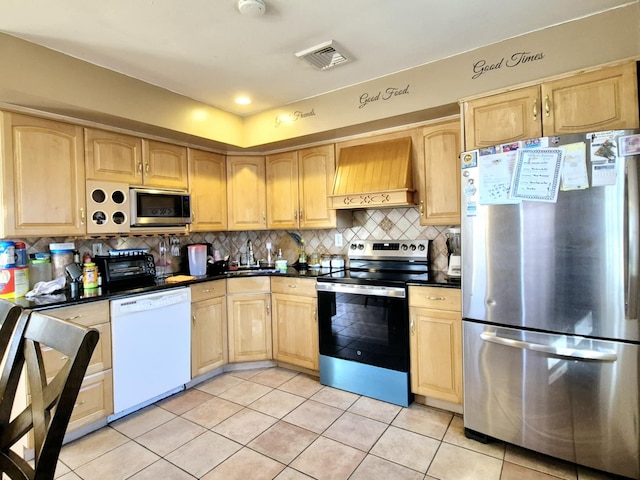 kitchen featuring visible vents, custom range hood, appliances with stainless steel finishes, light brown cabinetry, and backsplash