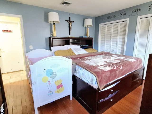 bedroom featuring multiple closets, visible vents, and wood finished floors