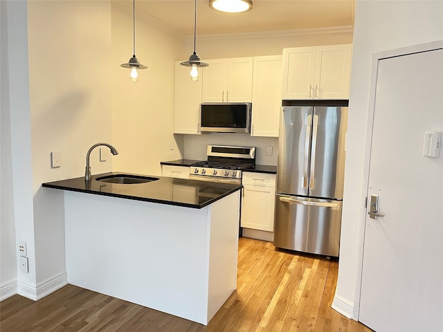 kitchen with dark countertops, appliances with stainless steel finishes, crown molding, light wood-style floors, and a sink