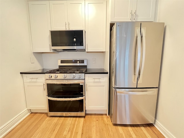 kitchen featuring appliances with stainless steel finishes, dark countertops, light wood-style flooring, and white cabinetry