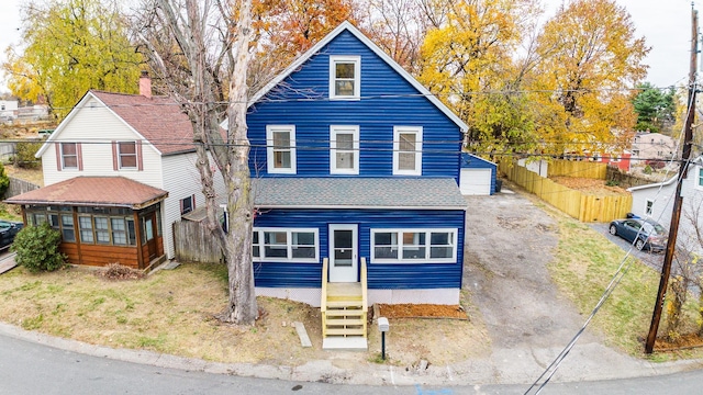 view of front of property featuring entry steps, driveway, fence, and roof with shingles