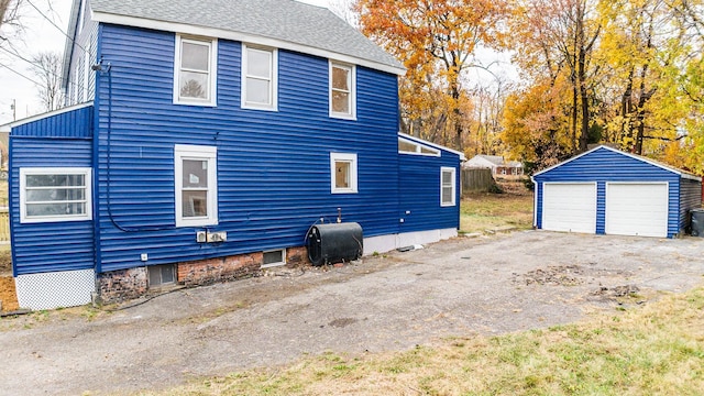 view of side of home with an outbuilding, a shingled roof, a detached garage, and heating fuel