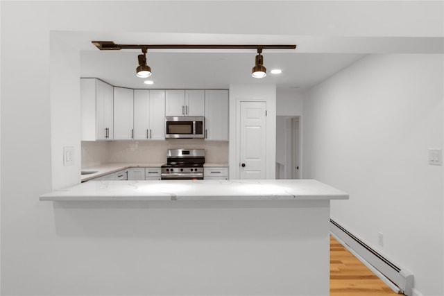 kitchen with tasteful backsplash, a peninsula, baseboard heating, stainless steel appliances, and white cabinetry