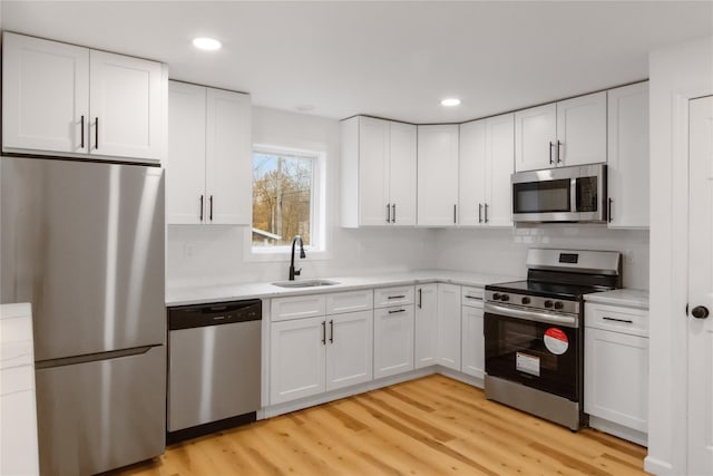 kitchen with appliances with stainless steel finishes, a sink, light wood-style floors, and white cabinets