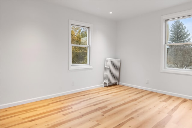 empty room featuring radiator heating unit, baseboards, wood finished floors, and recessed lighting