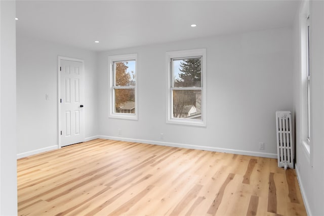 empty room with baseboards, recessed lighting, wood finished floors, and radiator