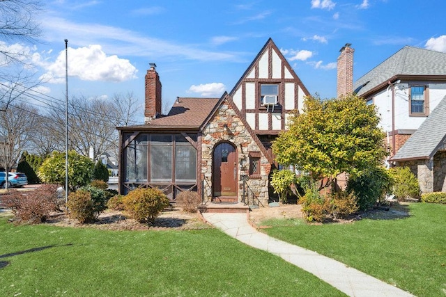 tudor home with a front yard, stone siding, a sunroom, and a chimney