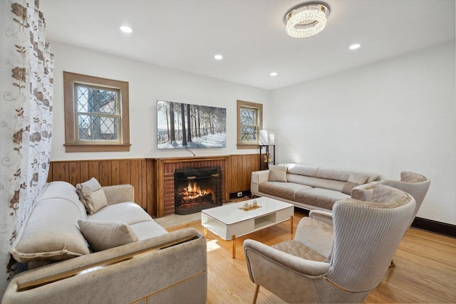 living room with light wood finished floors, a wainscoted wall, a fireplace, and a wealth of natural light