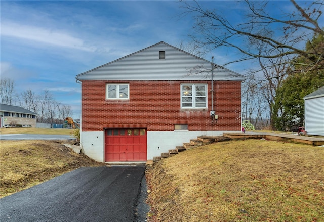 view of side of property with a yard, driveway, brick siding, and a garage