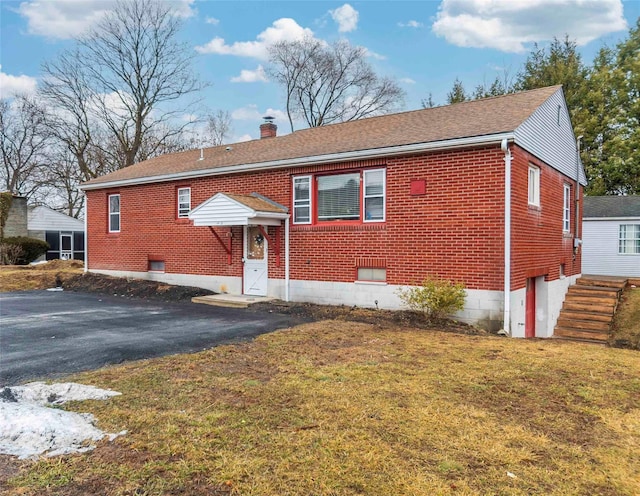 view of front of house featuring brick siding, a chimney, a front lawn, and aphalt driveway