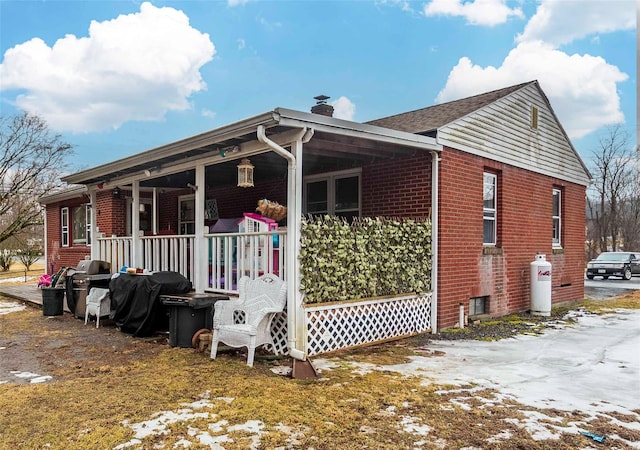 view of side of home with covered porch, brick siding, and a chimney