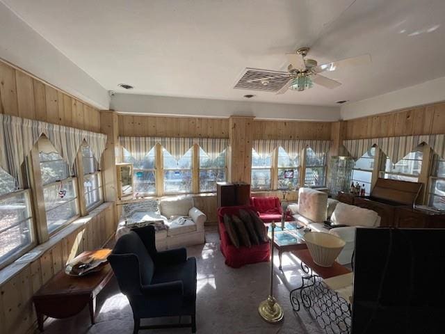 living area featuring wood walls, plenty of natural light, visible vents, and a ceiling fan