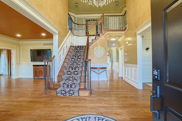 foyer entrance featuring ornamental molding, a decorative wall, stairway, and wood finished floors