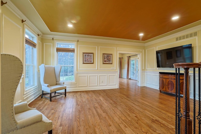 living area with recessed lighting, a decorative wall, visible vents, ornamental molding, and light wood-type flooring