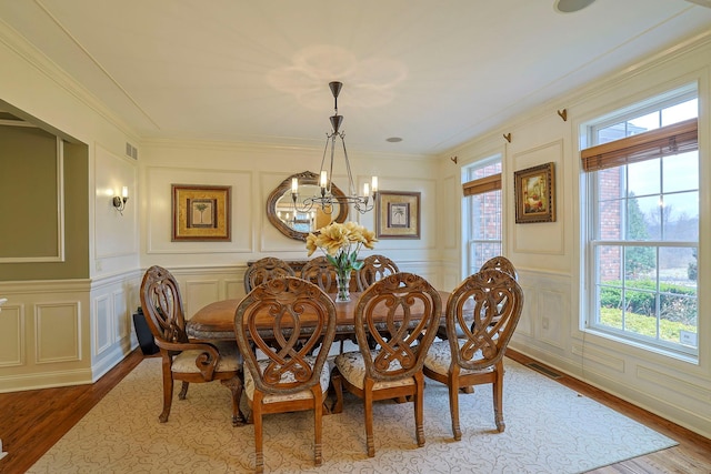 dining space featuring crown molding, a chandelier, a decorative wall, and wood finished floors