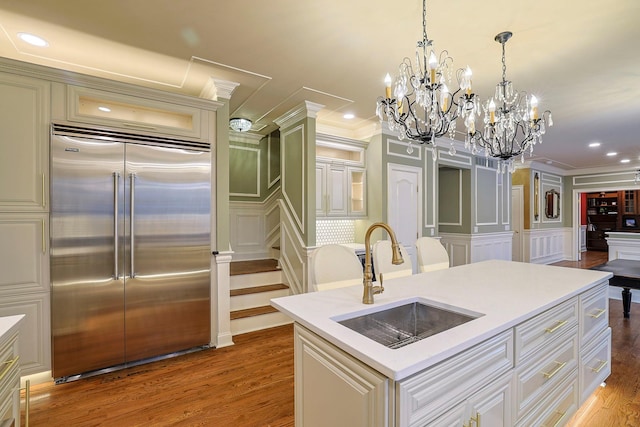 kitchen featuring stainless steel built in refrigerator, a sink, a decorative wall, and wood finished floors