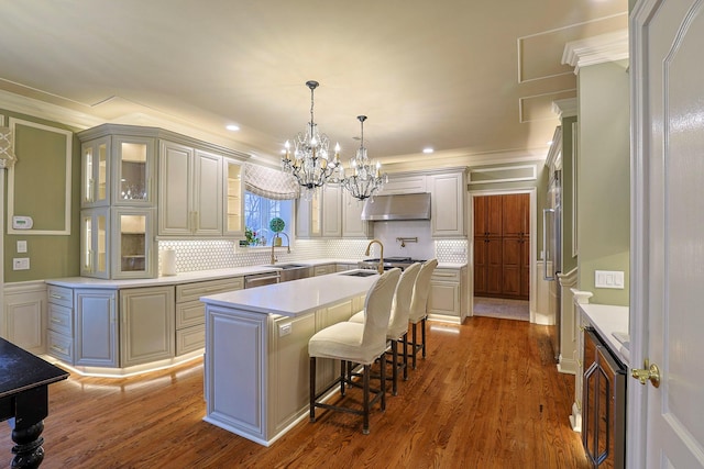 kitchen featuring under cabinet range hood, wood finished floors, a sink, light countertops, and a center island with sink