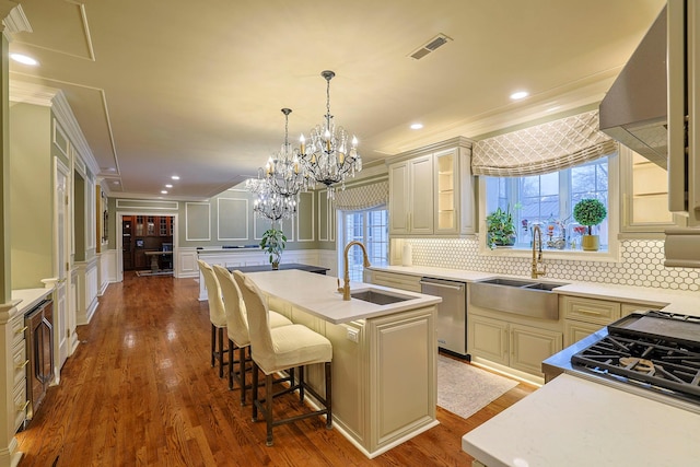 kitchen featuring cream cabinetry, crown molding, visible vents, a decorative wall, and a sink