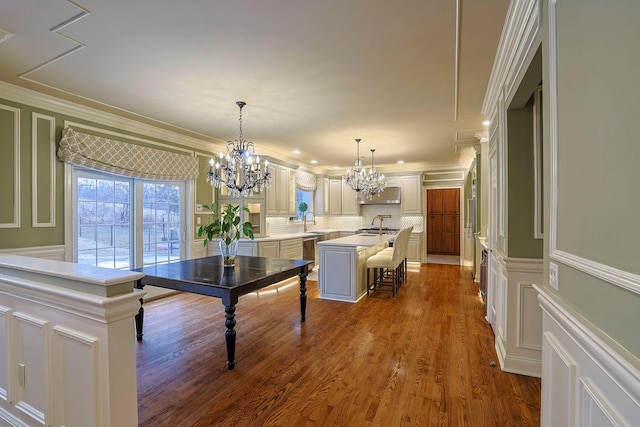 dining area featuring wainscoting, wood finished floors, an inviting chandelier, crown molding, and a decorative wall