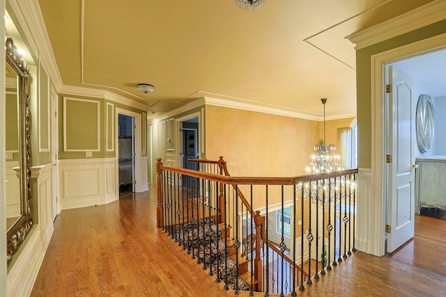 hallway with a chandelier, a decorative wall, an upstairs landing, and wood finished floors