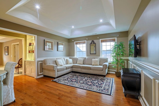 living area with a tray ceiling, a decorative wall, wood finished floors, and wainscoting