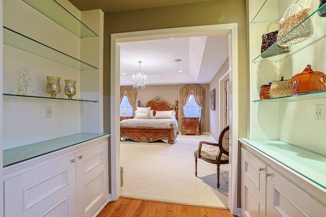 bedroom featuring a tray ceiling, light wood-style floors, light colored carpet, and a notable chandelier