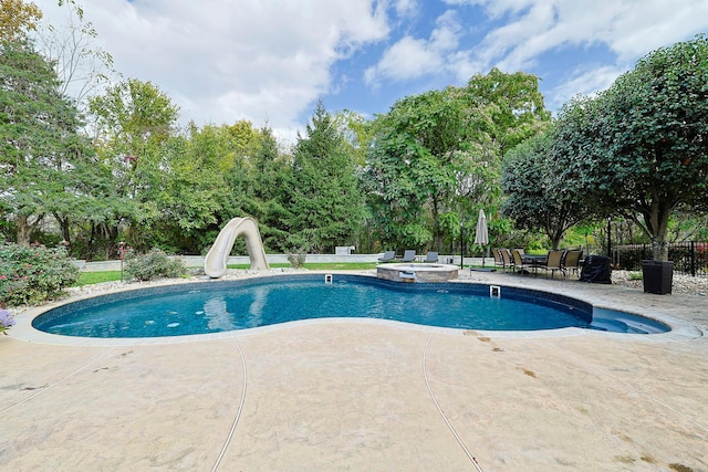 view of pool featuring a pool with connected hot tub, a water slide, a patio area, and fence