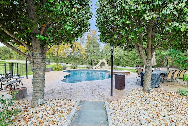 pool with a patio, a water slide, and fence