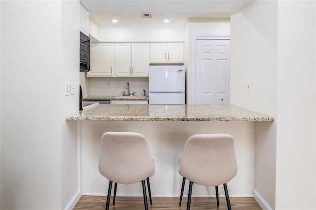 kitchen with light stone counters, visible vents, freestanding refrigerator, a sink, and a peninsula