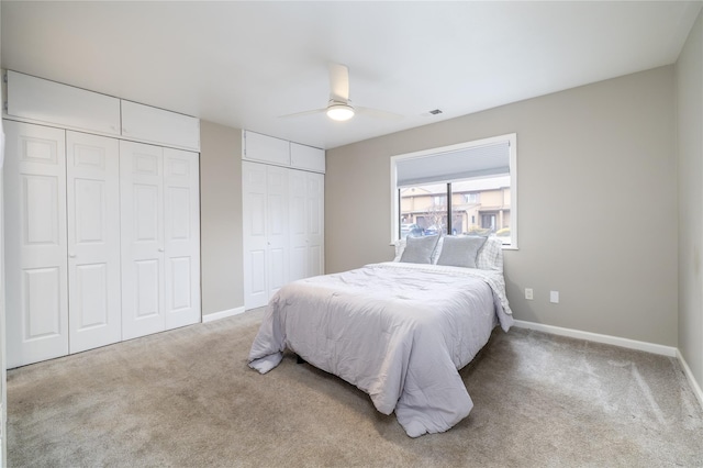 carpeted bedroom featuring ceiling fan, visible vents, baseboards, and two closets