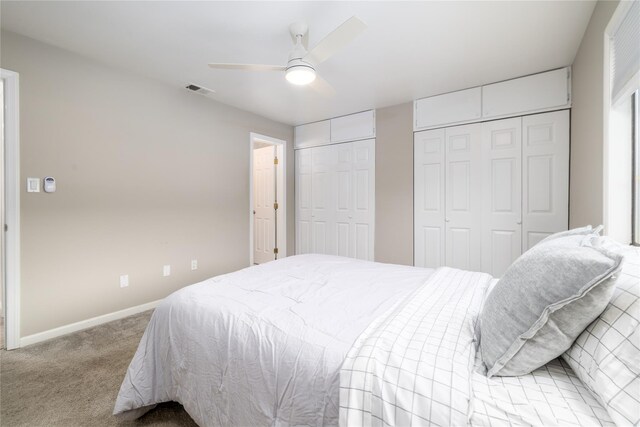 bedroom with multiple closets, light colored carpet, visible vents, a ceiling fan, and baseboards