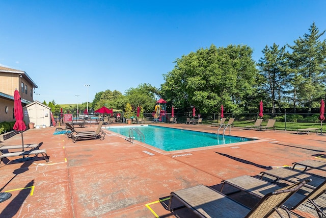 pool with a storage unit, a patio area, fence, and an outdoor structure