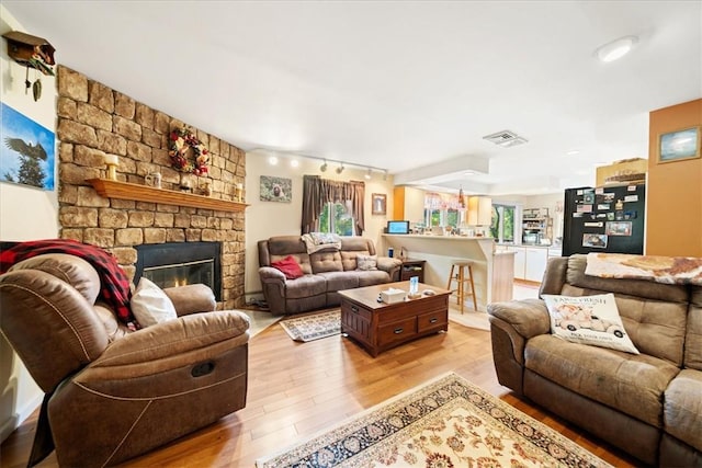 living area featuring a stone fireplace, light wood finished floors, rail lighting, and visible vents