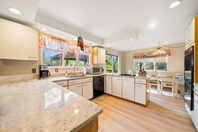 kitchen with light stone counters, light wood-style flooring, a sink, a peninsula, and black appliances