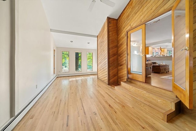 unfurnished room featuring a baseboard heating unit, wooden walls, ceiling fan, and light wood-style floors