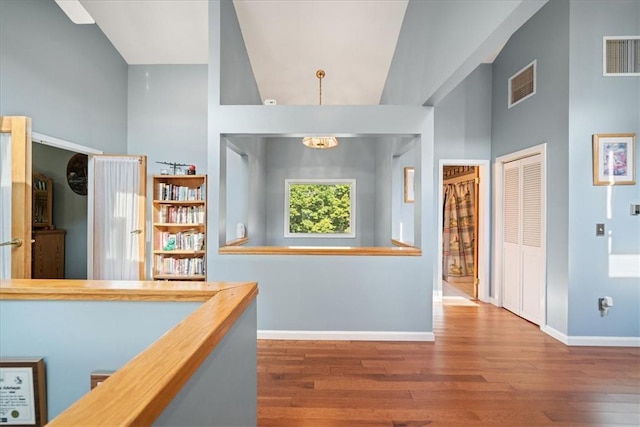 corridor featuring high vaulted ceiling, visible vents, baseboards, and wood finished floors