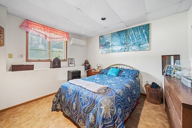 carpeted bedroom with a paneled ceiling, baseboards, and an AC wall unit