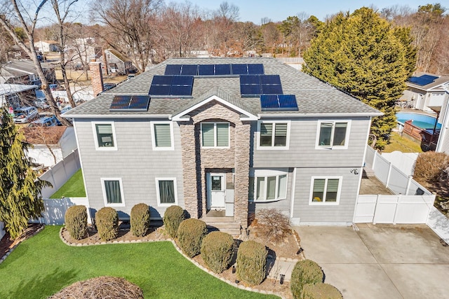 traditional-style home featuring a fenced backyard, roof mounted solar panels, a front lawn, and roof with shingles