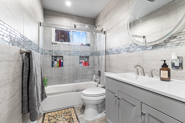 bathroom with combined bath / shower with glass door, tile walls, toilet, and vanity