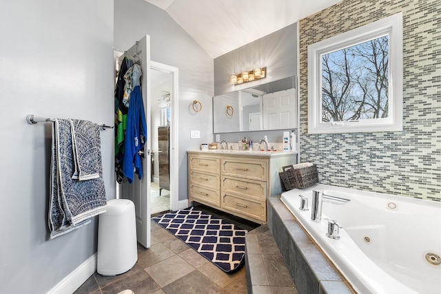 bathroom with lofted ceiling, baseboards, a tub with jets, and vanity