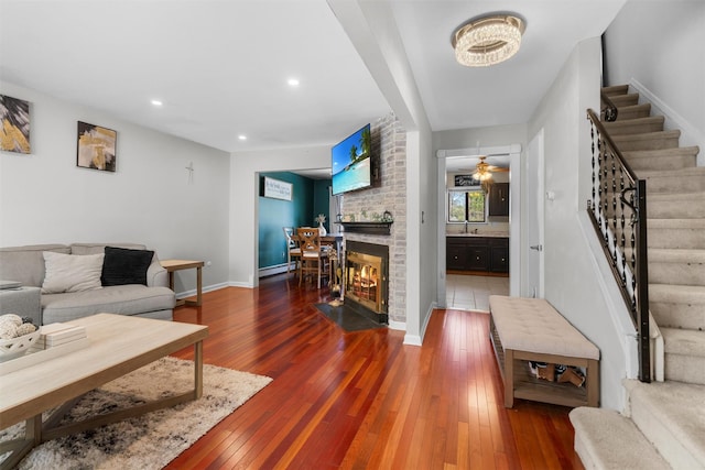 living room with stairway, a brick fireplace, baseboards, and wood-type flooring