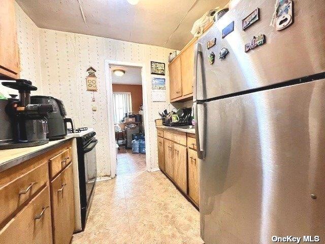 kitchen with black gas range, brown cabinets, freestanding refrigerator, and wallpapered walls