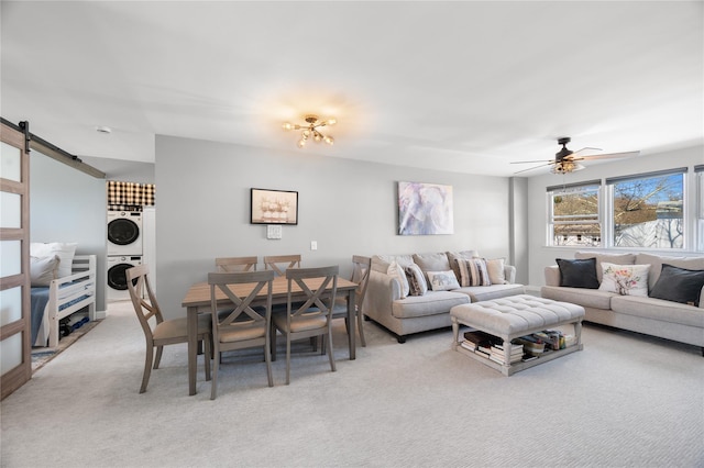 living room featuring a ceiling fan, light colored carpet, stacked washing maching and dryer, and a barn door