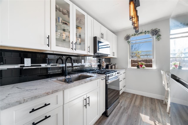 kitchen with light wood finished floors, light stone counters, glass insert cabinets, stainless steel appliances, and a sink